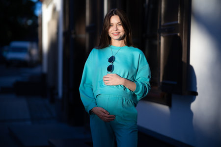 Portrait of a pretty attractive sexy young pregnant woman with natural makeup with beautiful eyes in a fashionable bright clothes. Girl is walking around the city.の写真素材
