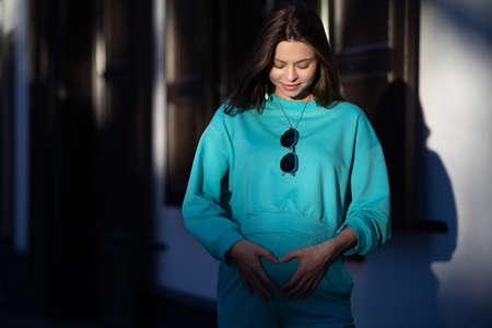 Portrait of a pretty attractive sexy young pregnant woman with natural makeup with beautiful eyes in a fashionable bright clothes. Girl is walking around the city.の写真素材