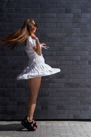 Fashionable women's portrait of a beautiful vogue girl pregnant model with fashion black eyewear in a stylish white short dress near a black brick wallの写真素材