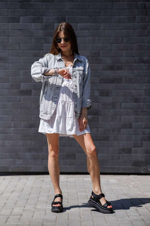 Fashionable women's portrait of a beautiful vogue girl pregnant model with fashion black eyewear in a stylish white short dress near a black brick wallの写真素材