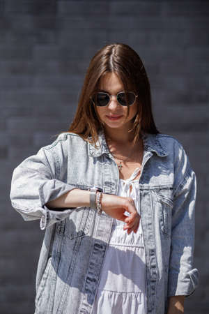 Fashionable women's portrait of a beautiful vogue girl pregnant model with fashion black eyewear in a stylish white short dress near a black brick wallの写真素材