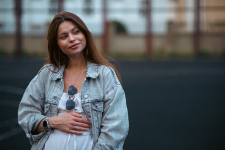 Beautiful young pregnant girl in a white dress and a denim jacket on a basketball court. The woman gently holds her hands on her stomach. The concept of pregnancy and sports.の写真素材