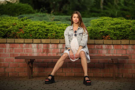 Gorgeous young pregnant woman in fashion jeans clothes in stylish dress has a good time in the park. Attractive girl model in casual outfit.の写真素材