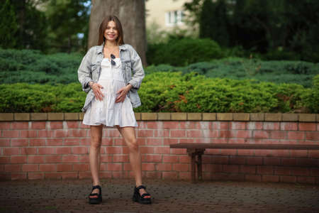 Gorgeous young pregnant woman in fashion jeans clothes in stylish dress has a good time in the park. Attractive girl model in casual outfit.の写真素材