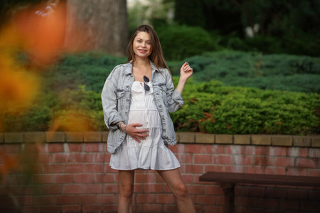 Gorgeous young pregnant woman in fashion jeans clothes in stylish dress has a good time in the park. Attractive girl model in casual outfit.の写真素材
