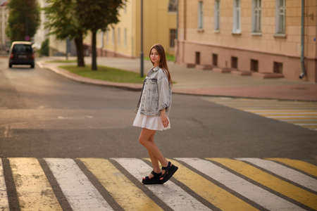 Beautiful happy pregnant woman in a vintage fashion jeans jacket and white dress walking in the city.の写真素材