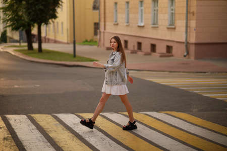 Beautiful happy pregnant woman in a vintage fashion jeans jacket and white dress walking in the city.の写真素材