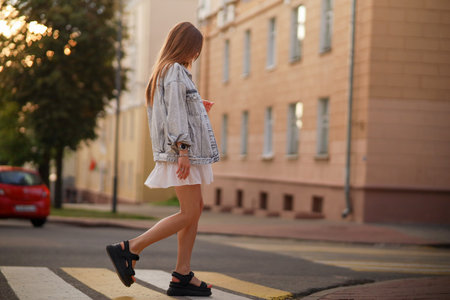Beautiful happy pregnant woman in a vintage fashion jeans jacket and white dress walking in the city.の写真素材