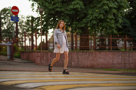 Beautiful happy pregnant woman in a vintage fashion jeans jacket and white dress walking in the city.の写真素材