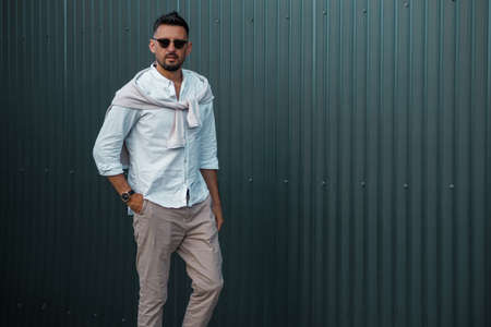 Fashion model handsome young man with trendy hairstyle in sunglasses in white shirt in light jeans...