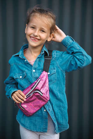 A cute smiling girl in a denim shirt poses on a dark background.の写真素材