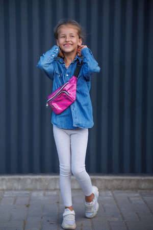 A cute smiling girl in a denim shirt poses on a dark background.の写真素材