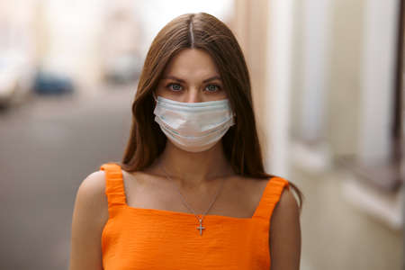 Girl, young woman in protective sterile medical mask on her face looking at camera outdoors close up. corona virus pandemic. Beautiful brunette haired girl with medical mask.の写真素材