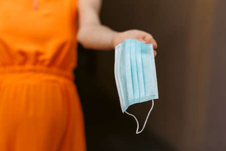 A young girl holds a medical mask in her hands. Suggests wearing a protective mask to protect against the virus.の写真素材