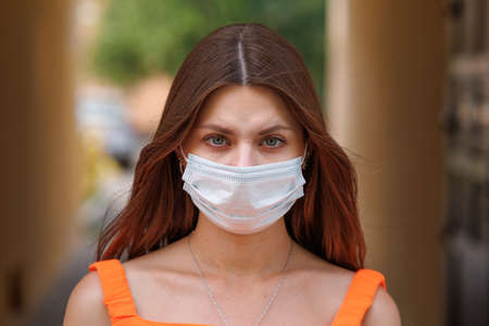 Girl, young woman in protective sterile medical mask on her face looking at camera outdoors close up. corona virus pandemic. Beautiful brunette haired girl with medical mask.の写真素材