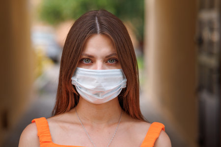 Girl, young woman in protective sterile medical mask on her face looking at camera outdoors close up. corona virus pandemic. Beautiful brunette haired girl with medical mask.の写真素材