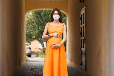 Girl, young woman in protective sterile medical mask on her face looking at camera outdoors close up. corona virus pandemic. Beautiful brunette haired girl with medical mask.の写真素材