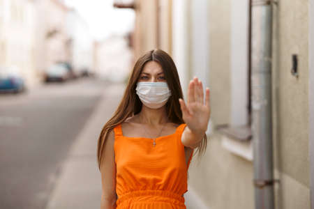 Girl, young woman in protective sterile medical mask on her face looking at camera outdoors close up. corona virus pandemic. Beautiful brunette haired girl with medical mask.の写真素材