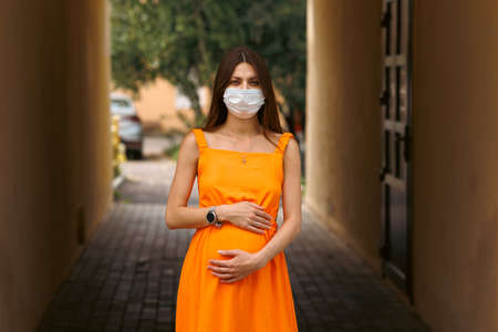 Girl, young woman in protective sterile medical mask on her face looking at camera outdoors close up. corona virus pandemic. Beautiful brunette haired girl with medical mask.の写真素材