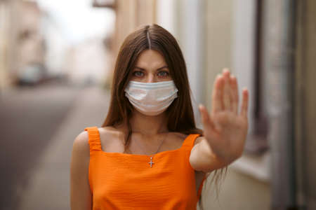 Girl, young woman in protective sterile medical mask on her face looking at camera outdoors close up. corona virus pandemic. Beautiful brunette haired girl with medical mask.の写真素材