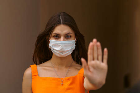 Girl, young woman in protective sterile medical mask on her face looking at camera outdoors close up. corona virus pandemic. Beautiful brunette haired girl with medical mask.の写真素材
