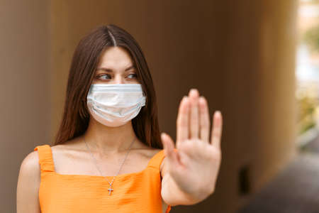 Girl, young woman in protective sterile medical mask on her face looking at camera outdoors close up. corona virus pandemic. Beautiful brunette haired girl with medical mask.の写真素材