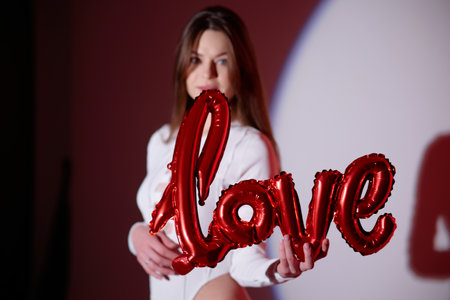 Beautiful young woman with red balloons in the shape of the word loveの写真素材