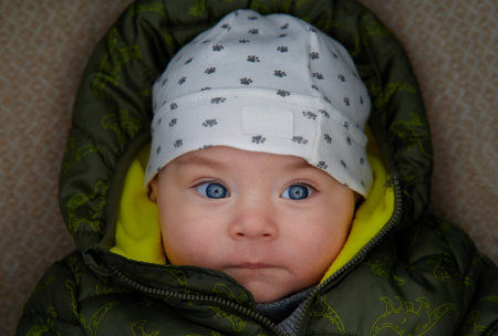 Portrait of a newborn baby boy with blue eyes wearing a hat and green jacketの写真素材