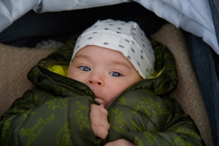 Portrait of a cute newborn baby boy with blue eyes wearing a green down jacketの写真素材