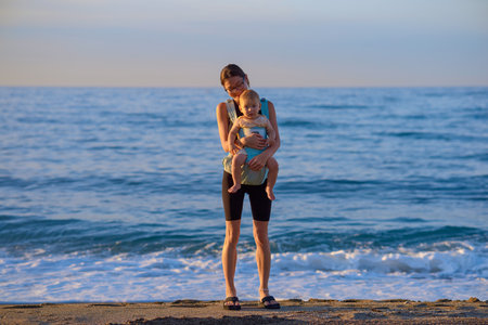 Young mother and her little daughter on the beach at the sunset.の写真素材