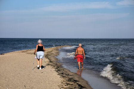 Senior couple walking on the beach in summertime, looking at each otherの写真素材