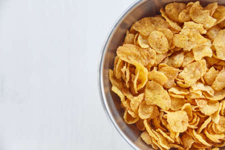 Cornflakes in a metal bowl on a painted white wooden background. Free space for lettering.