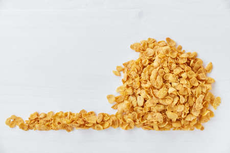 Heap of cornflakes on a painted white wooden background. Free space for lettering.