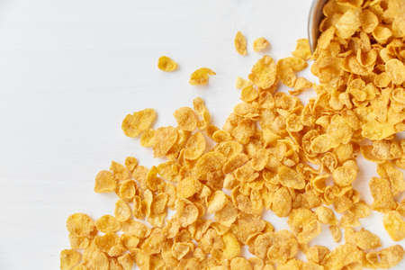 Placer of cornflakes with a metal bowl on a painted white wooden background. Cornflakes scattered on a wooden table.の写真素材