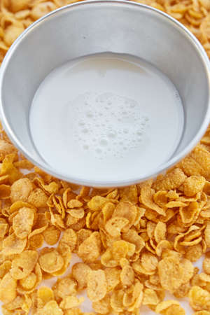 Metal bowl with milk on a painted white wooden background. Cornflakes scattered on a wooden table.の写真素材