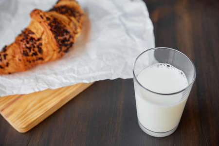 Freshly baked croissant on a dark wooden table. Fresh croissant on white crumpled paper and a wooden board with a glass of milk.の写真素材