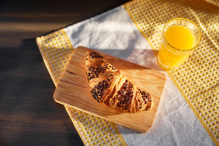Freshly baked croissant on a dark wooden table. Fresh croissant on a wooden board and kitchen towel with a cup of orange juice.の写真素材
