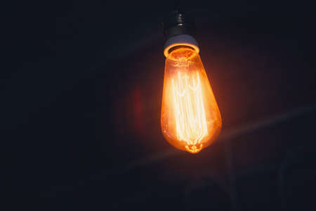 A bright warm orange lamp of Edison on a dark cold background. Soft processing and toning of photos. A vintage bulb hangs on the cordの写真素材