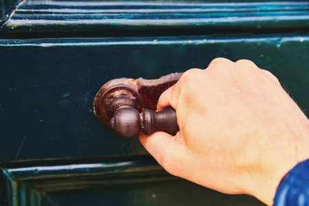 A man's hand opens the door, a close-up photo. The hand holds onto the antique metal handle of the green-blue doorの写真素材