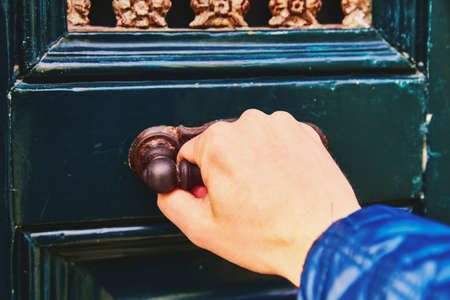 A man's hand opens the door, a close-up photo. The hand holds onto the antique metal handle of the green-blue doorの写真素材