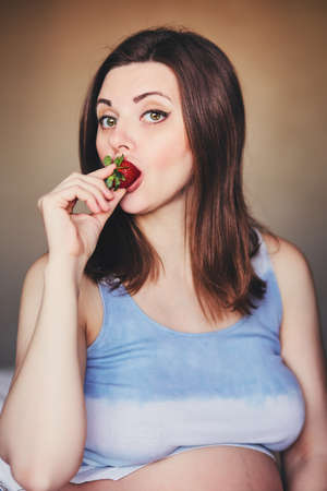 Portrait of an attractive pregnant woman who bites sucking a large ripe strawberry. Healthy eating...