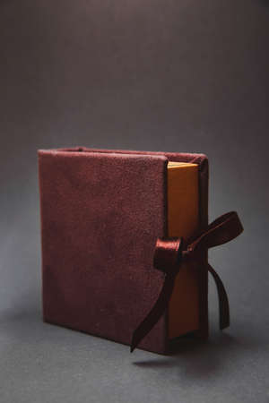 Dark brown box for a flash drive with a cover from a suede, tied to satin ribbons with a bow. A beautiful stylish luxury gift package on a dark background. A gift for respectable wealthy peopleの写真素材