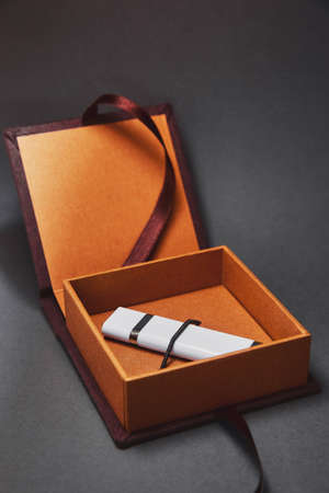 A dark brown box for USB flash drive with a cover made of suede is open with a flash drive inside. A beautiful stylish luxury gift package on a dark background. A gift for respectable wealthy peopleの写真素材