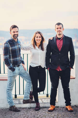 Two men and one woman are standing next to smile and joke, have fun. Friends laugh at the background...