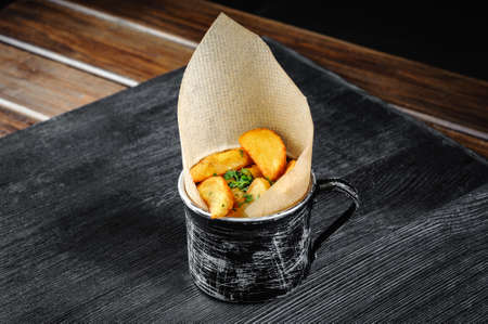 Potatoes fried in mug. Black wood background