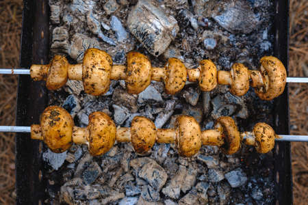 Grilled mushrooms on skewers cooked in a brazier, close-up.