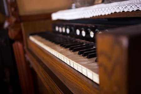 Selective focus on the keyboard on an old rustic piano. There are lace tablecloths on the piano. The piano is very old and quite used.の写真素材