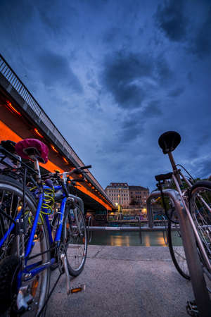 The bikes were parked in a bicycle parking lot next to the bridge on the Danube canal in Vienna. It's dusk and the sky is very gloomy.の写真素材