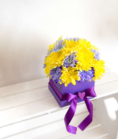 Beautiful decoration of chrysanthemum flowers. The flowers are yellow and purple and are in the handmade box with the bow also purple. Behind is a white background.の写真素材