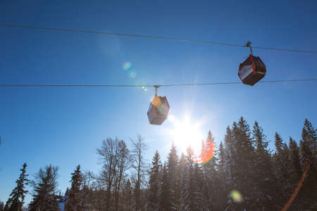 It's a beautiful sunny day on the mountain. There are two gondolas on the cable car and behind them...